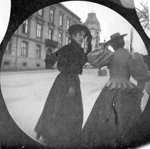 Two women walking. One turns her head to look at the photographer; perhaps he called to her so he could photograph her face