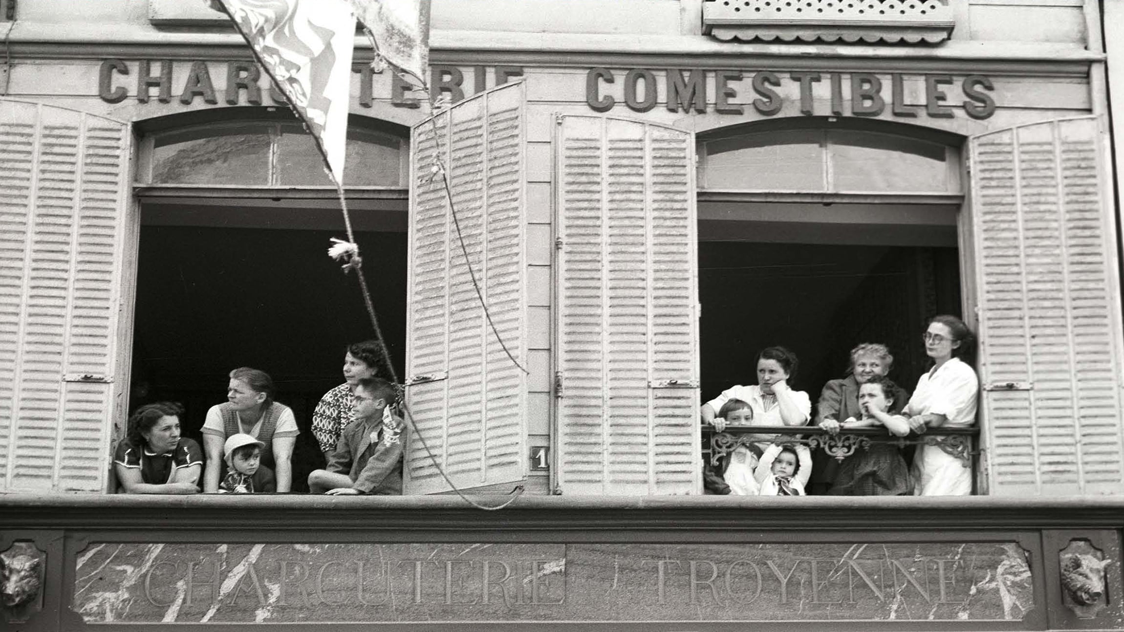 La famille Boillon aux fenêtres de leur appartement regarde passer le Tour en 1954. Photo publiée avec l'aimable autorisation de Pierre Boillon, colorisée et améliorée avec les outils de MyHeritage.<br />

