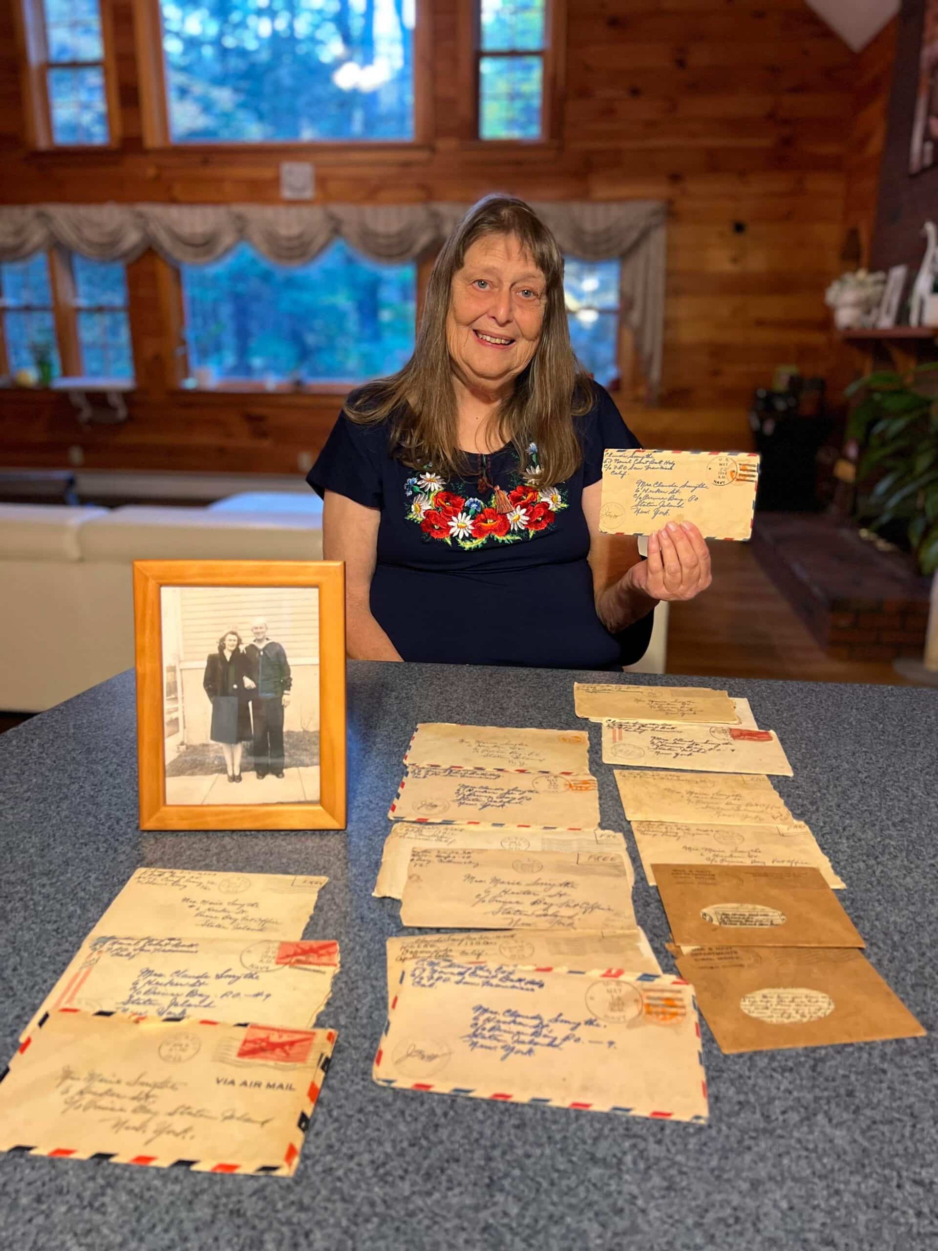 Carol holding the letters with a photo of her parents on the table