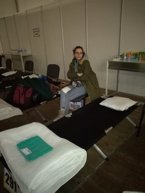 Photo of Ukrainian woman at refugee center, seated among a row of cots