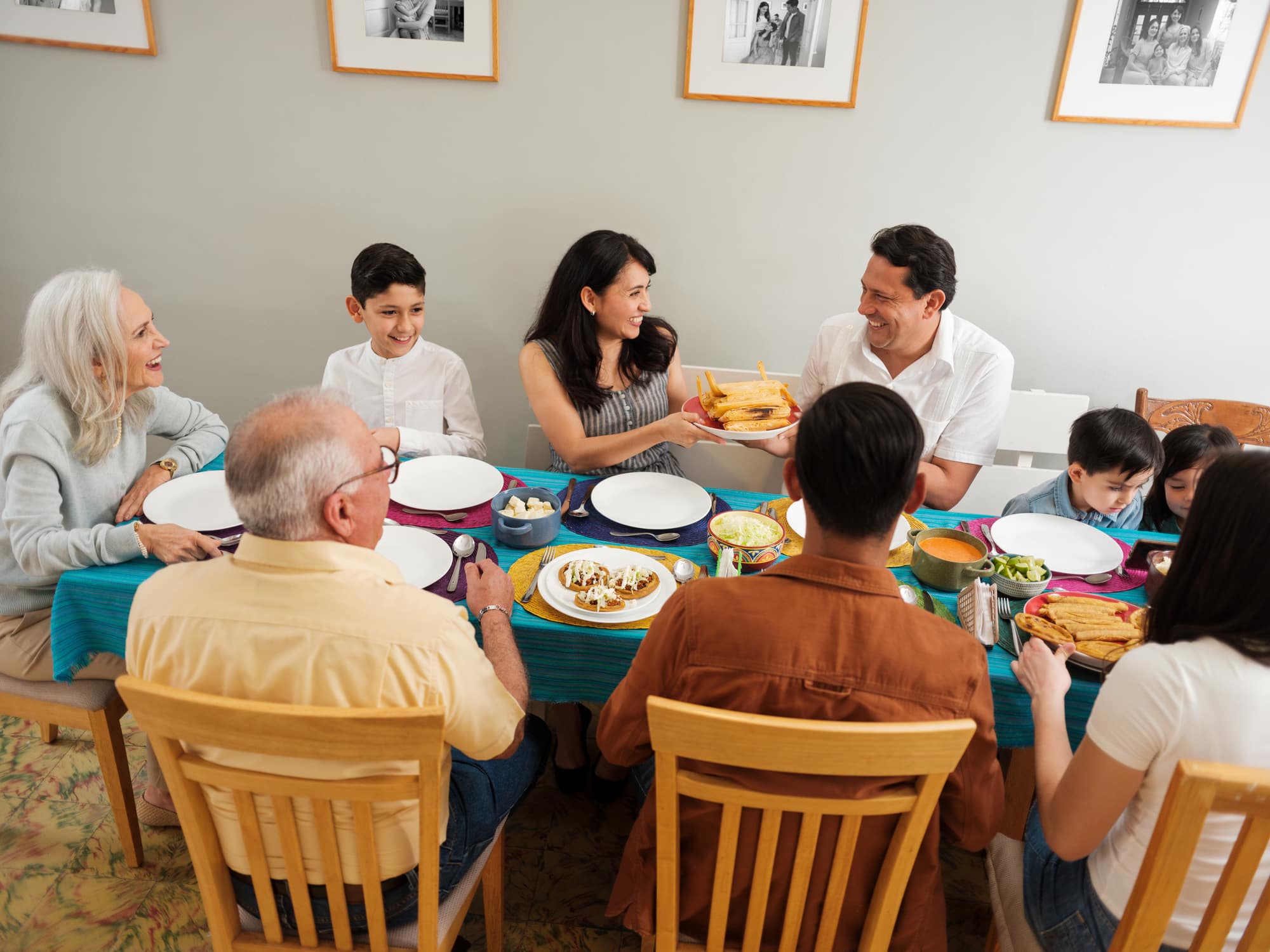 A happy intergenerational mexican family passing food to each other at the table and smiling.