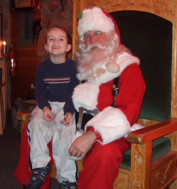 Glücklicher kleiner Junge auf dem Schoß des Weihnachtsmanns. Foto verbessert und Farben restauriert mit MyHeritage